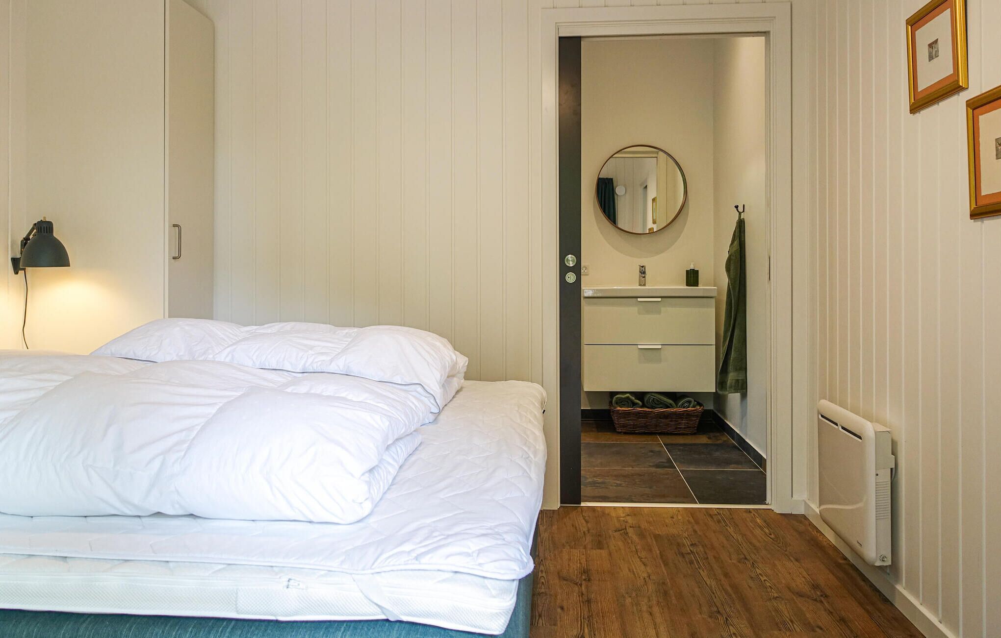 Une chambre à coucher avec un lit, une lampe de chevet, un miroir et une petite salle de bain comprenant un lavabo et un porte-serviettes.