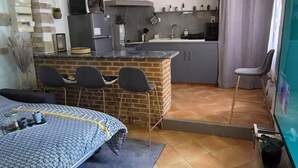 Een compacte keuken met een centraal eiland, een eetgedeelte met een tafel met dessin, en een woonruimte met een televisie.