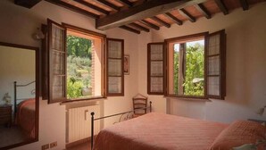 Une chambre avec un grand lit, des poutres en bois au plafond et deux fenêtres équipées de volets.