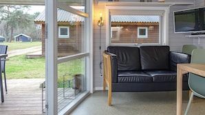 Un salon moderne avec un canapé en cuir noir, une table à manger en bois et un téléviseur fixé au mur.