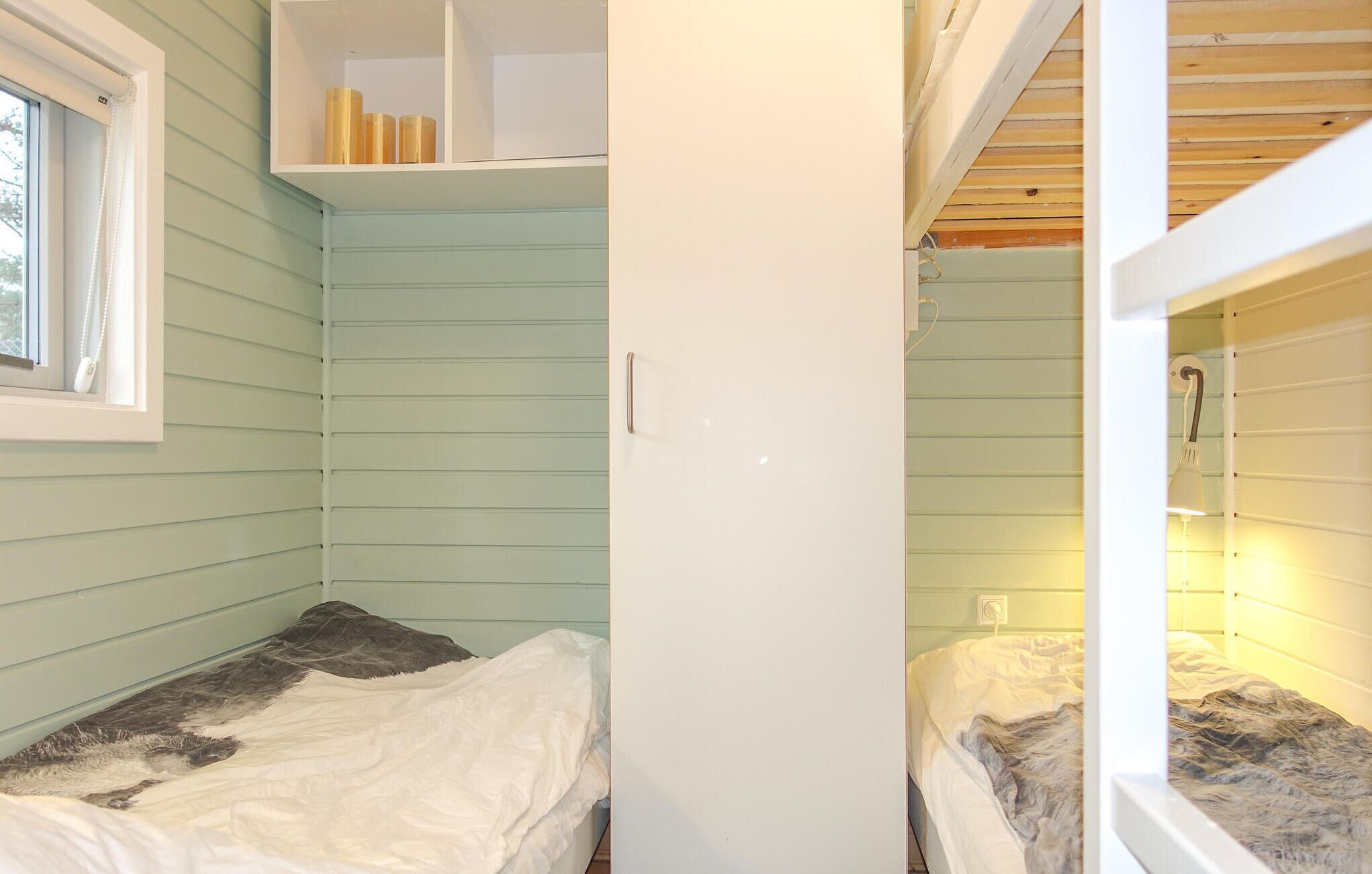 Quarto pequeno e compacto com duas camas, uma janela e uma estante com livros.