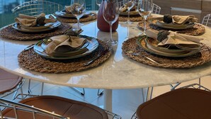 Une table ronde, dressée pour le dîner, avec des assiettes, des couverts et des verres, entourée de sets de table en fibres tressées et agrémentée d’un vase de fleurs.
