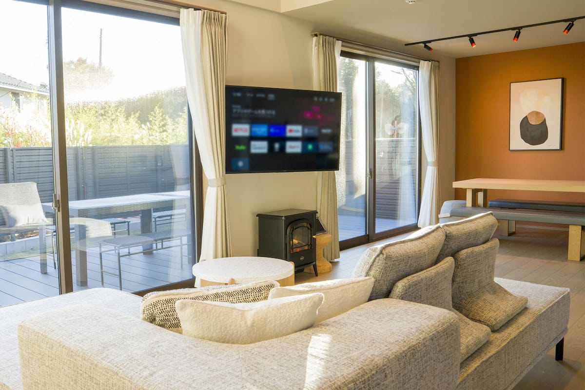 Ein modernes Wohnzimmer mit einer großen Couch, einem flachbildfernseher, der an der Wand befestigt ist, und einer Schiebetür zu einem Außenbereich mit Terrasse.