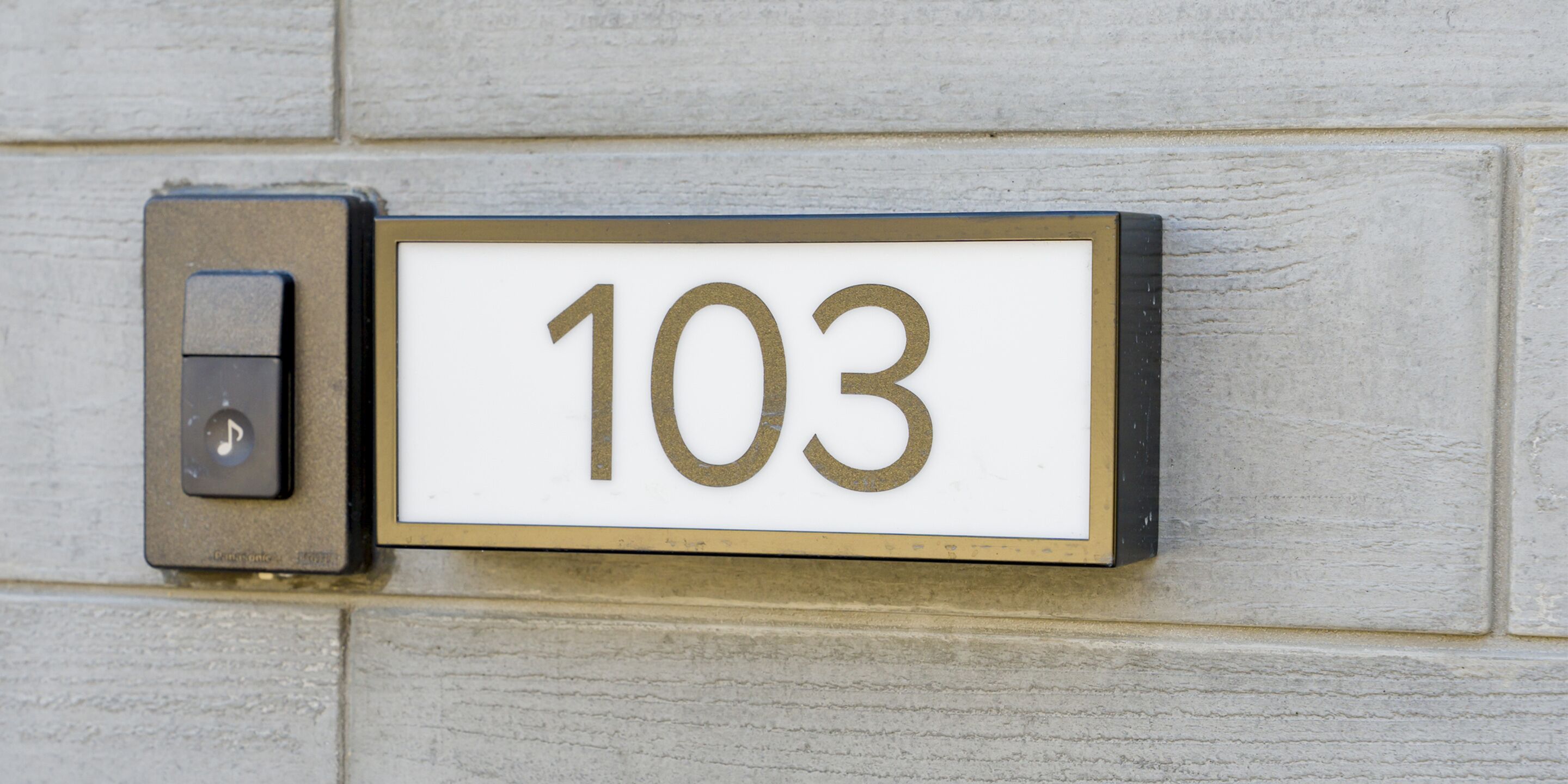 A house number sign, 103, mounted on a light-colored brick wall.