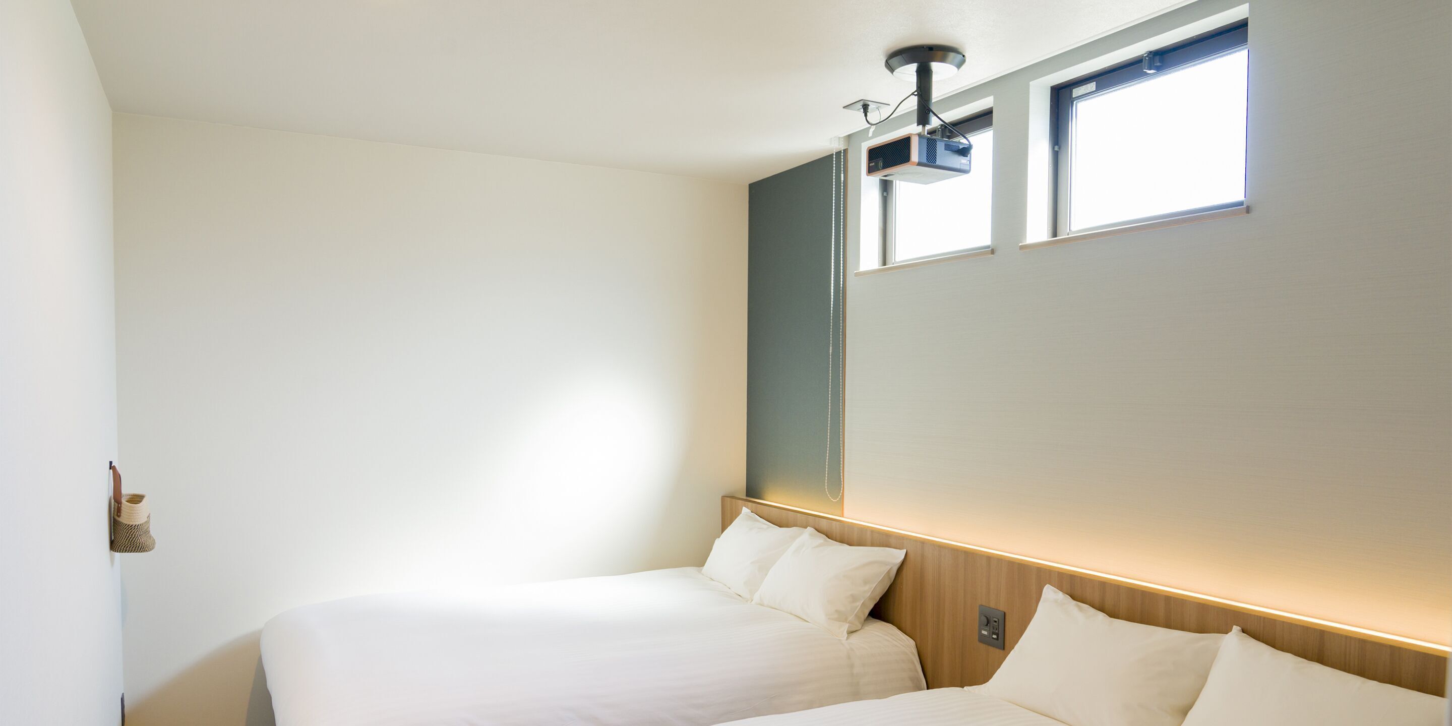A hotel room with a bed, a wall-mounted projector, and a window.