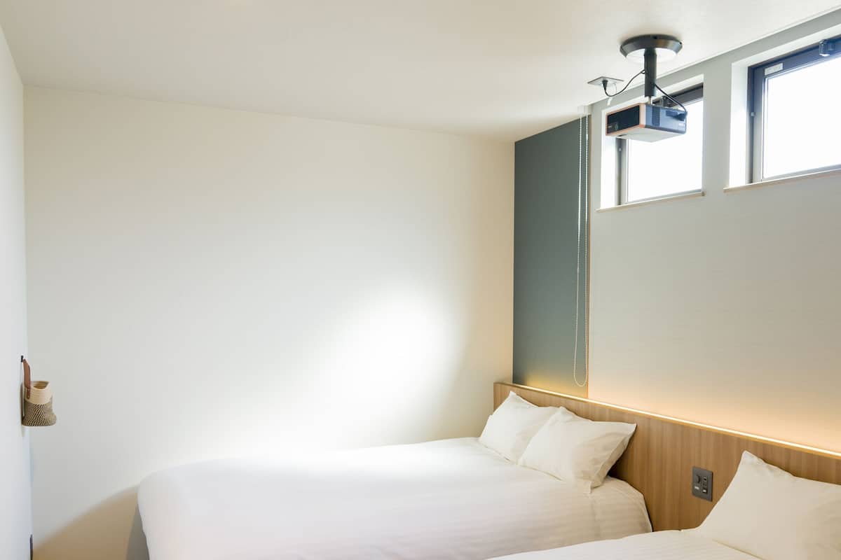 Ein Hotelzimmer mit Bett, einem an der Wand befestigten Projektor und einem Fenster.