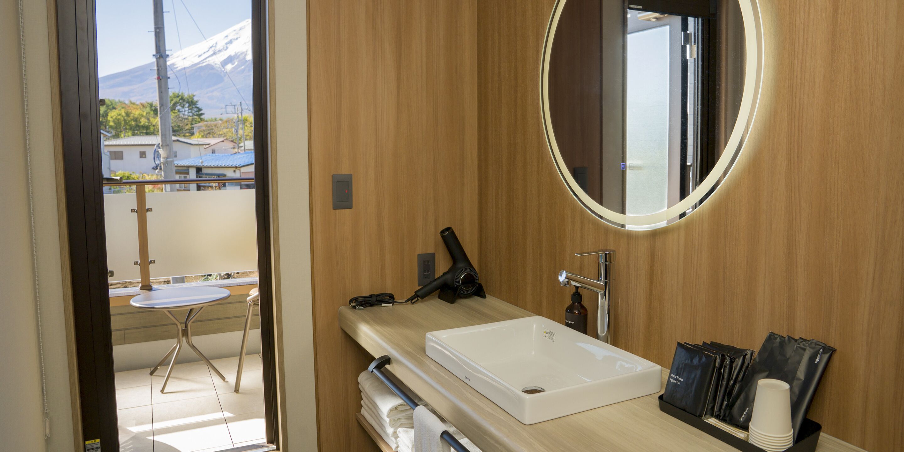 Un baño moderno con un tocador de madera, un lavabo, un espejo y una pequeña mesa con una silla.