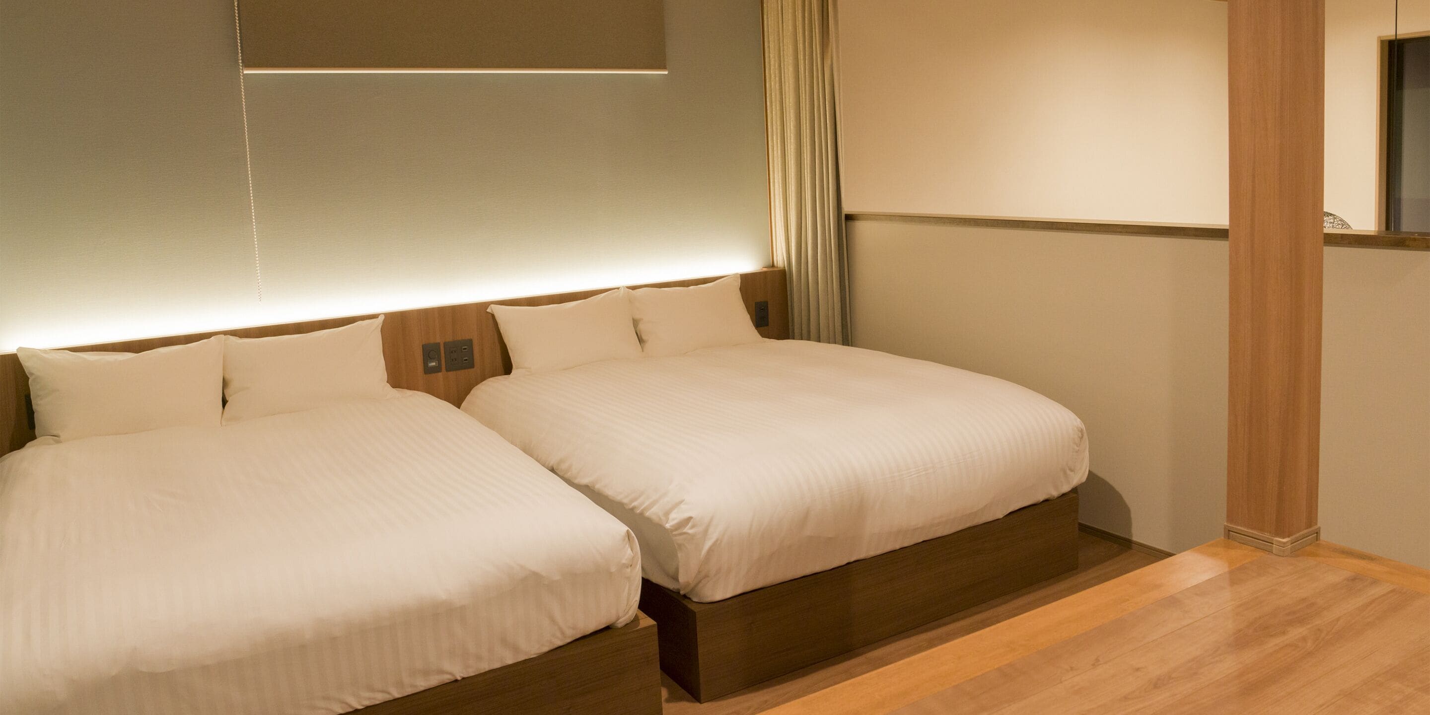 Habitación de hotel con dos camas, piso de madera y una paleta de colores neutros.