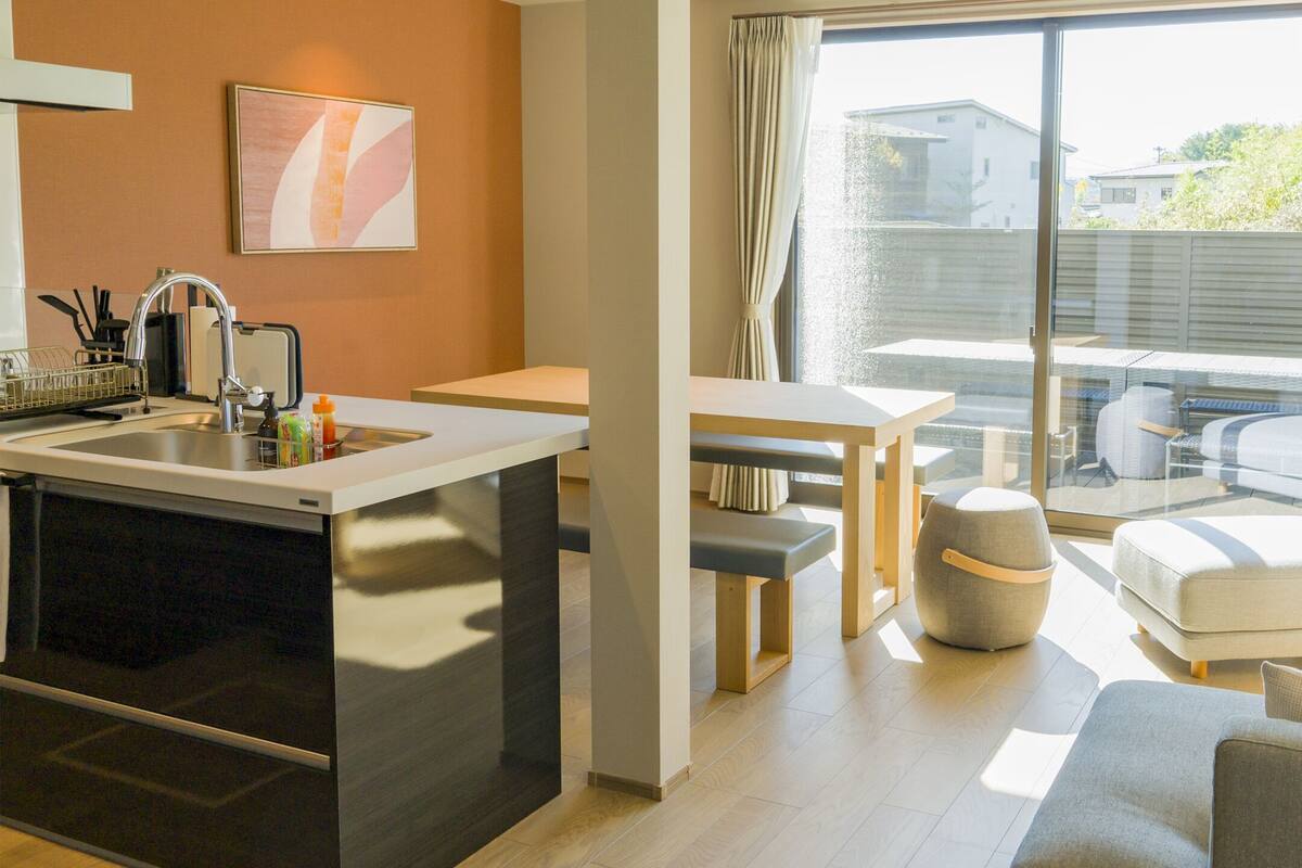 Eine moderne Küche mit Einbauofen, ein Essbereich mit Tisch und Bänken, ein Sofa und ein an der Wand befestigter Fernseher.