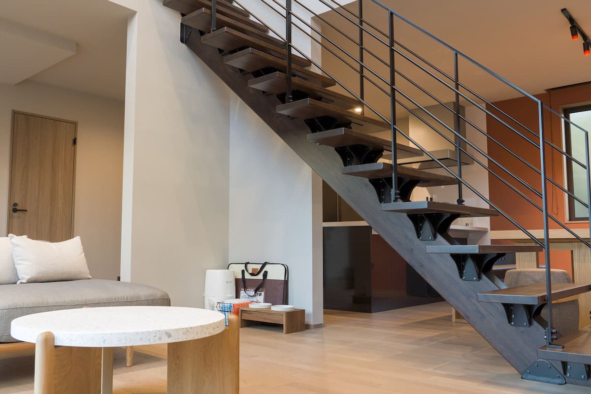 Ein modernes Wohnzimmer mit einem grauen Sofa, einem runden Couchtisch und einer Holztreppe mit Metallgeländern.