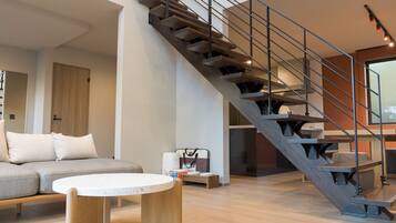A modern living room with a grey sofa, a round coffee table, and a wooden staircase with metal railings.