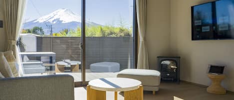 A modern living room with a large sliding glass door leading to a balcony, a flat-screen TV mounted on the wall, and a cozy seating area with a round wooden table.