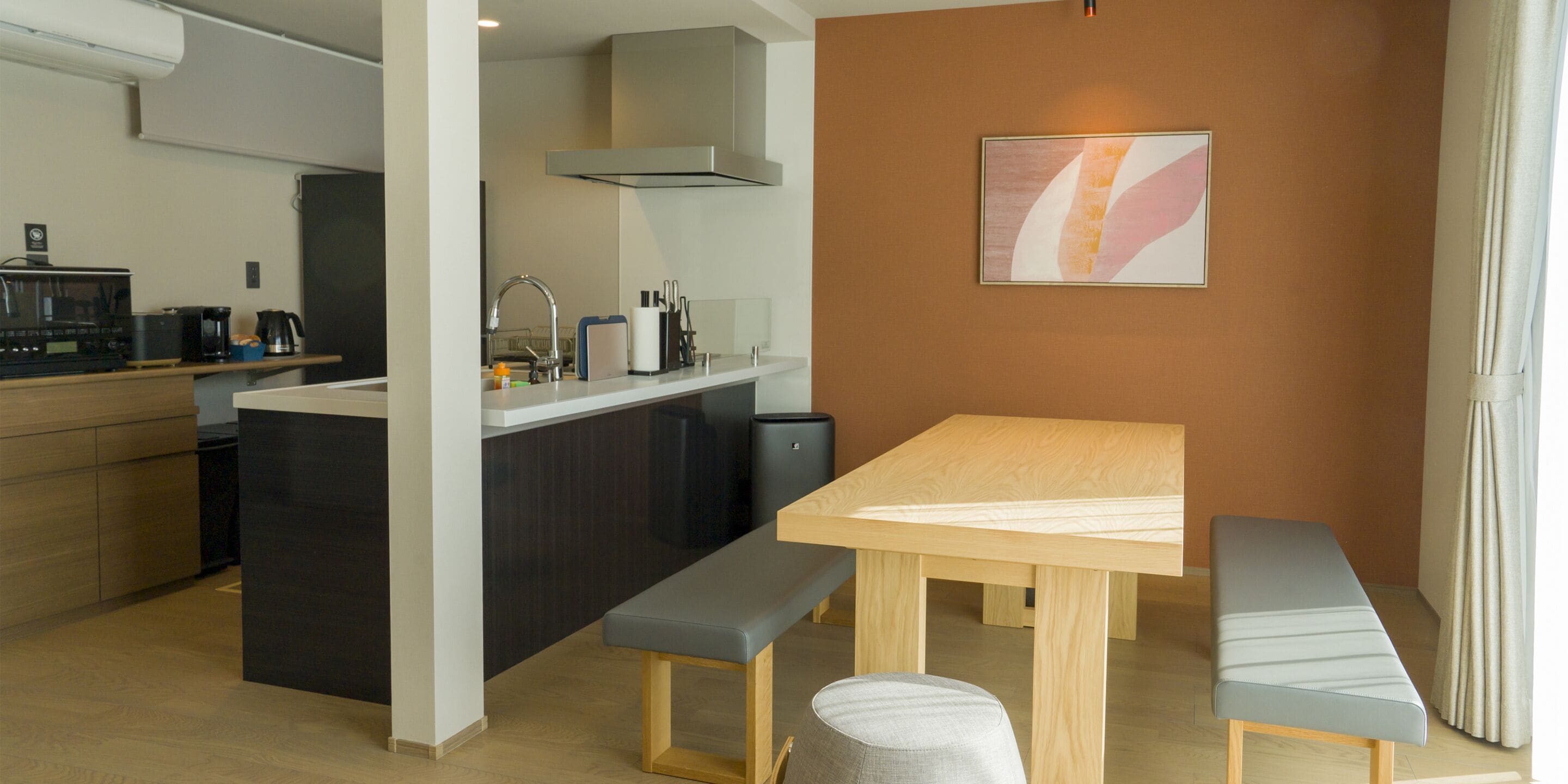 A modern kitchen with a wooden table and bench, a small island with a sink, and a kitchen counter with appliances.