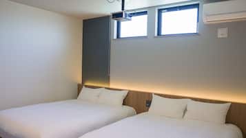 A hotel room with two beds, a ceiling-mounted projector, and an air conditioning unit.