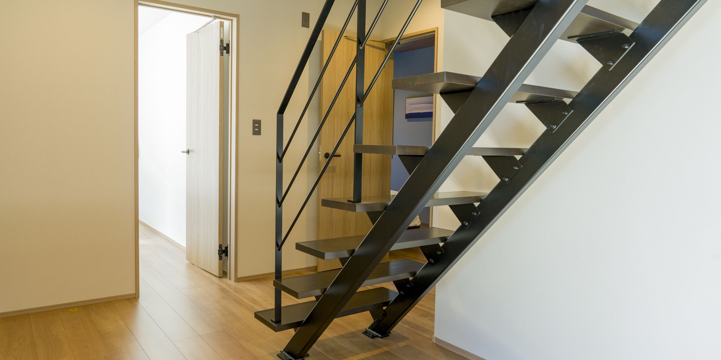 A modern staircase with a black metal railing and wooden steps, leading to a door.