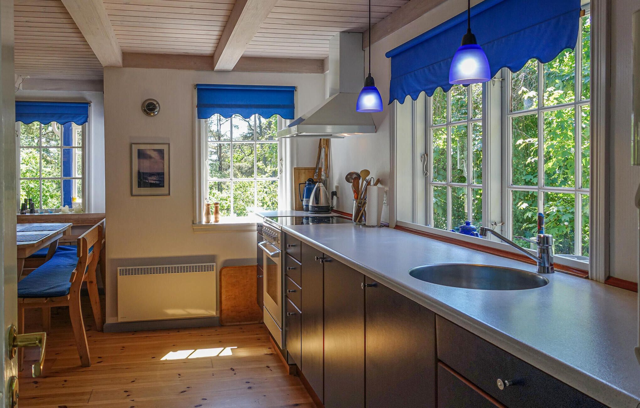 A kitchen with wooden flooring, a sink, cabinets, and a window with blue curtains.