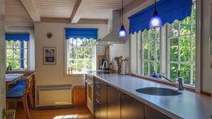 A kitchen with wooden flooring, a sink, cabinets, and a window with blue curtains. - Beautiful home in Nexø with sauna (Nexø)