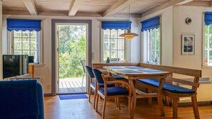 A cozy room with a wooden table and chairs, a television, and large windows with blue curtains. - Beautiful home in Nexø with sauna (Nexø)