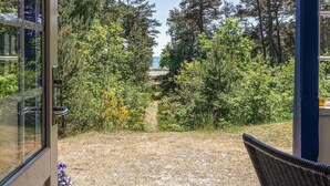 A view from a room with a glass door leading to a garden with a path, surrounded by trees and a body of water in the distance. - Beautiful home in Nexø with sauna (Nexø)