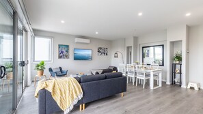 Un salon moderne avec un canapé, une table à manger et des chaises. Les murs sont ornés d’œuvres d’art, il y a un téléviseur et une grande fenêtre offrant une belle vue.