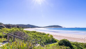 A beach with a wooden staircase leading down to the shore, surrounded by greenery. - Fingal Bay Seabreeze Unit 2  16 Tuna Crescent (Fingal Bay)