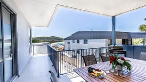A balcony with a wooden table set for a meal, overlooking a beach and a residential area. - Fingal Bay Seabreeze Unit 2  16 Tuna Crescent (Fingal Bay)