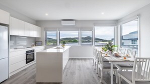 A modern kitchen with a central island, white cabinetry, and large windows offering a view of the sea and hills. - Fingal Bay Seabreeze Unit 2  16 Tuna Crescent (Fingal Bay)