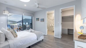 A modern bedroom with a large bed, a balcony with a table and chairs, and a walk-in closet. - Fingal Bay Seabreeze Unit 2  16 Tuna Crescent (Fingal Bay)