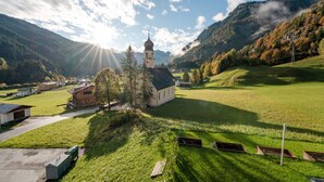 Une église dotée d’un clocher, entourée d’une vallée verdoyante et de montagnes.