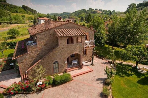 A stone building with a tiled roof, a balcony, and a small patio area with a table and chairs.