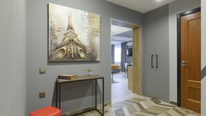 A hallway with a large painting of the Eiffel Tower, a red bench, a console table with a book and vase, and a wooden door.