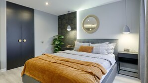 A modern bedroom with a large bed, a bedside table, a nightstand, a mirror, and a wardrobe.