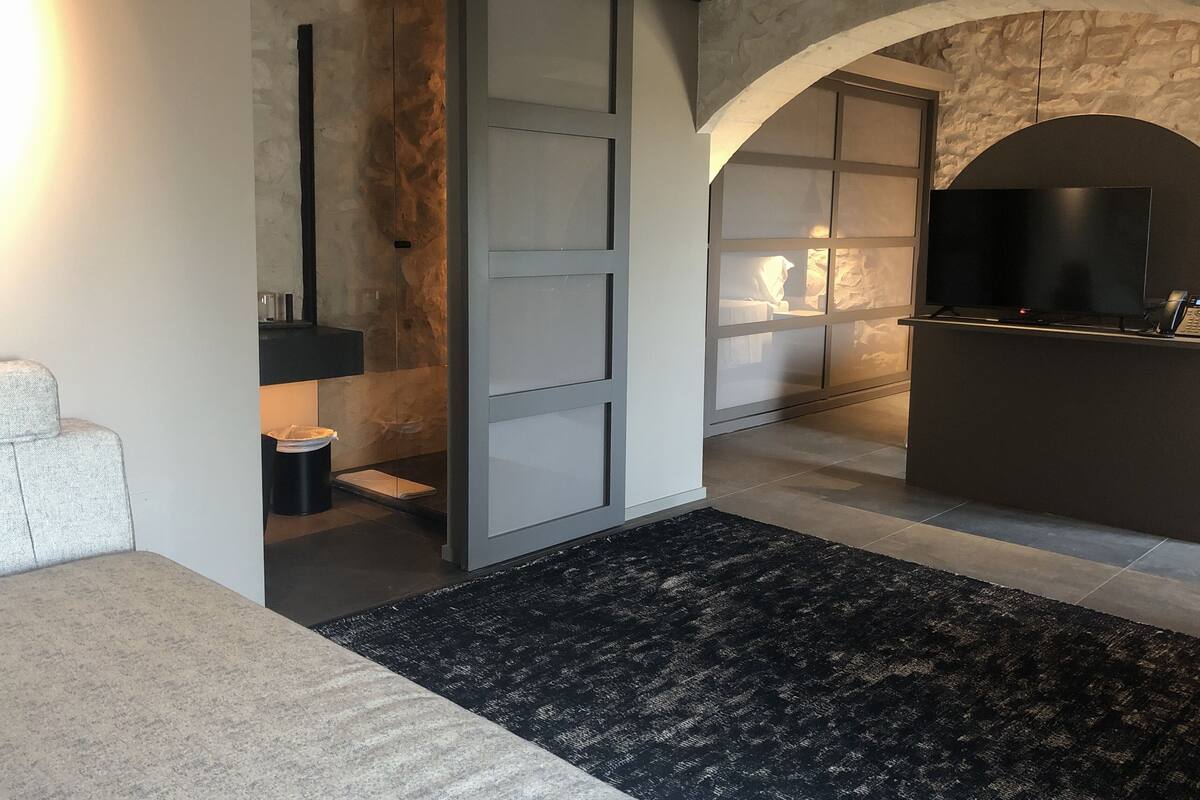 A modern living room with a large black rug, a sofa, a TV, and a stone wall.