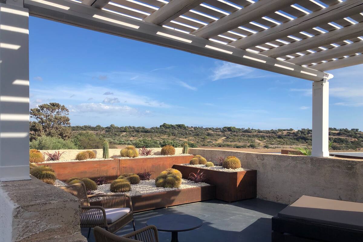 A covered outdoor seating area with a view of a landscaped garden and distant hills.