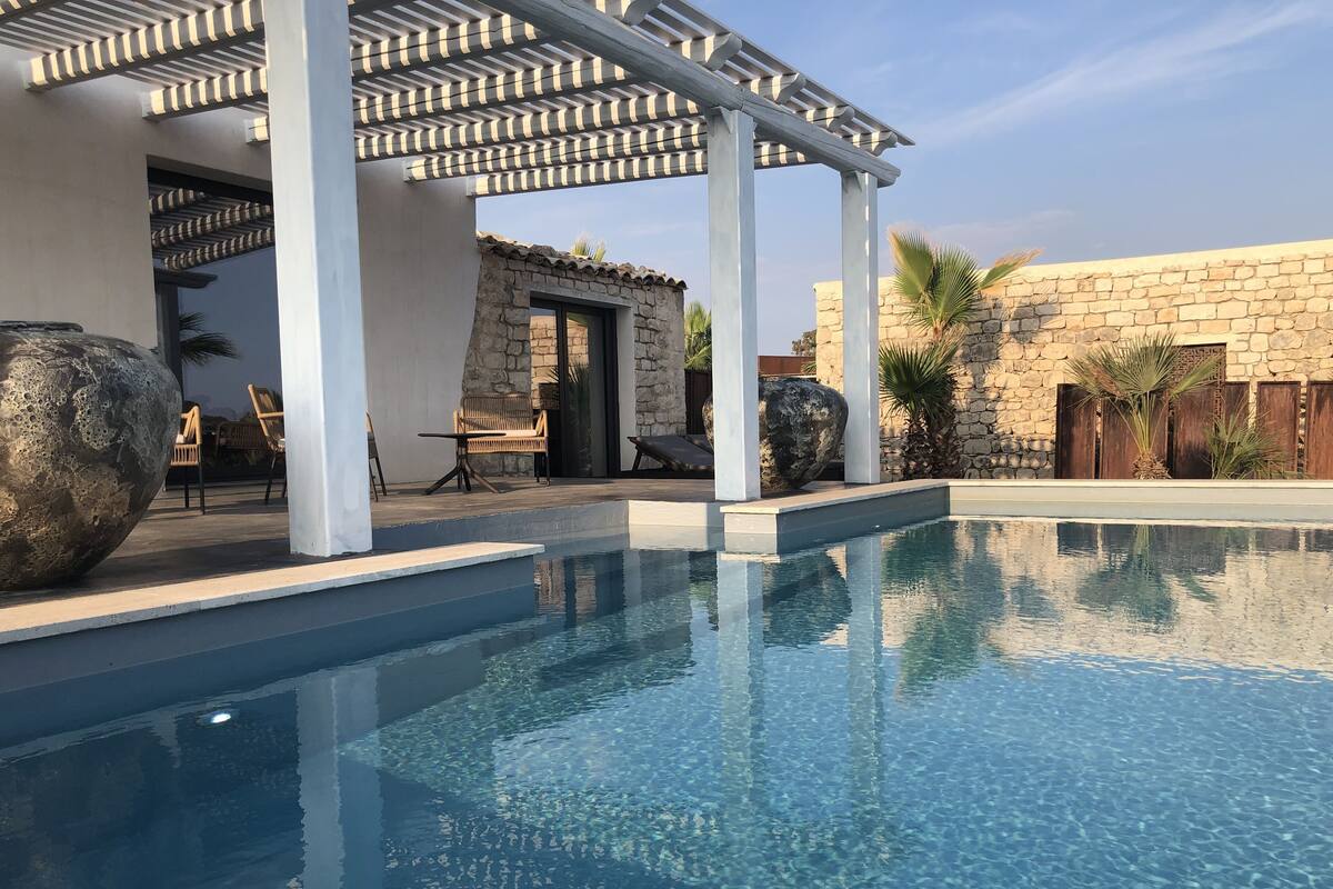A clear blue pool with a pergola overhead, stone walls, and outdoor seating.