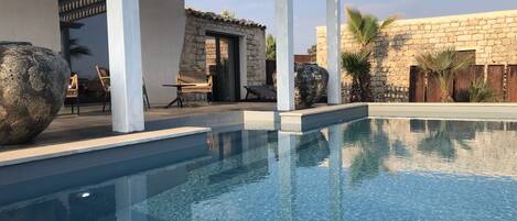 Une piscine d’un bleu éclatant, surmontée d’une pergola, avec des murs en pierre et des espaces de détente en plein air.
