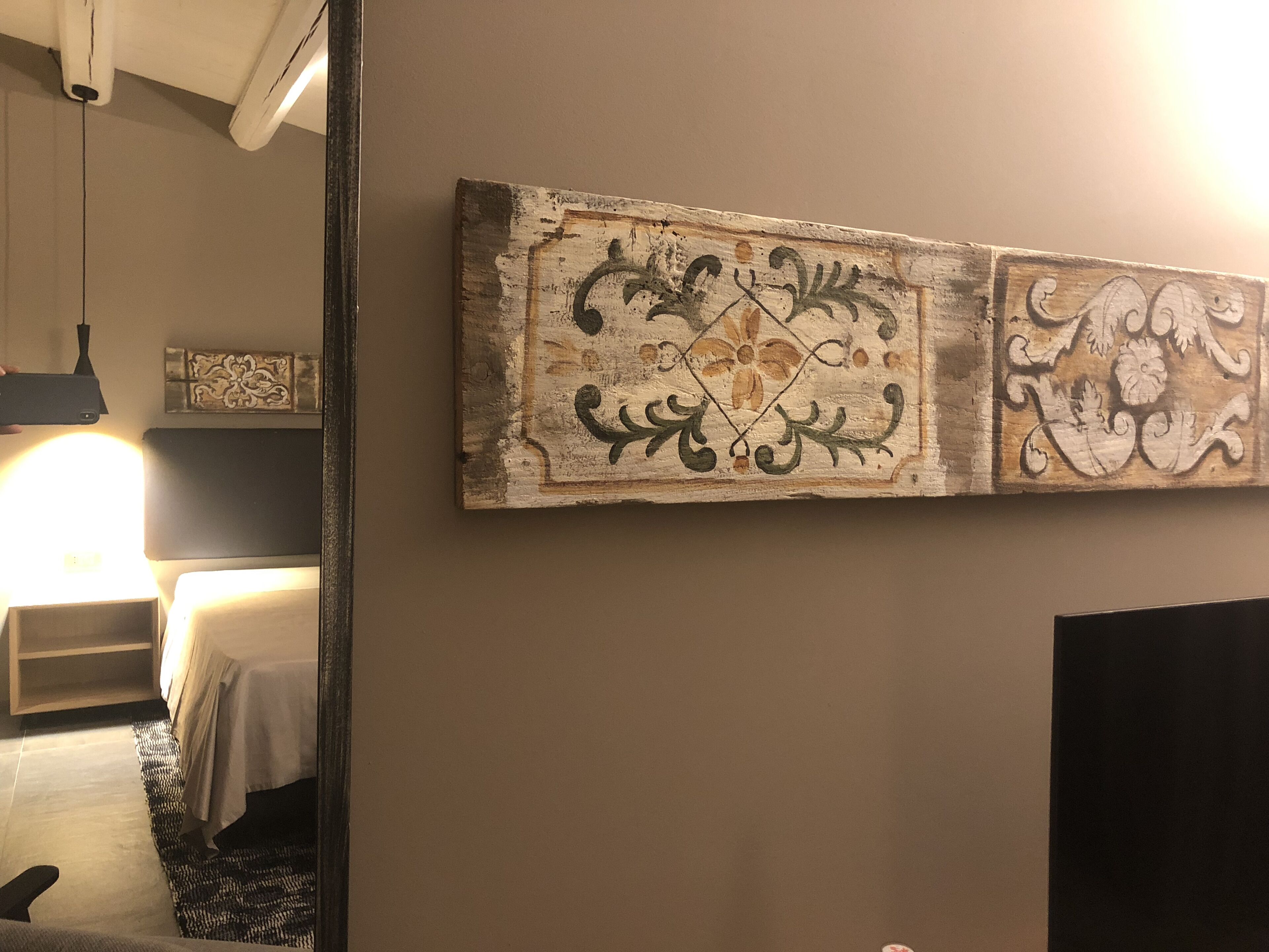 A hotel room with a bed, bedside table, and a large mirror.