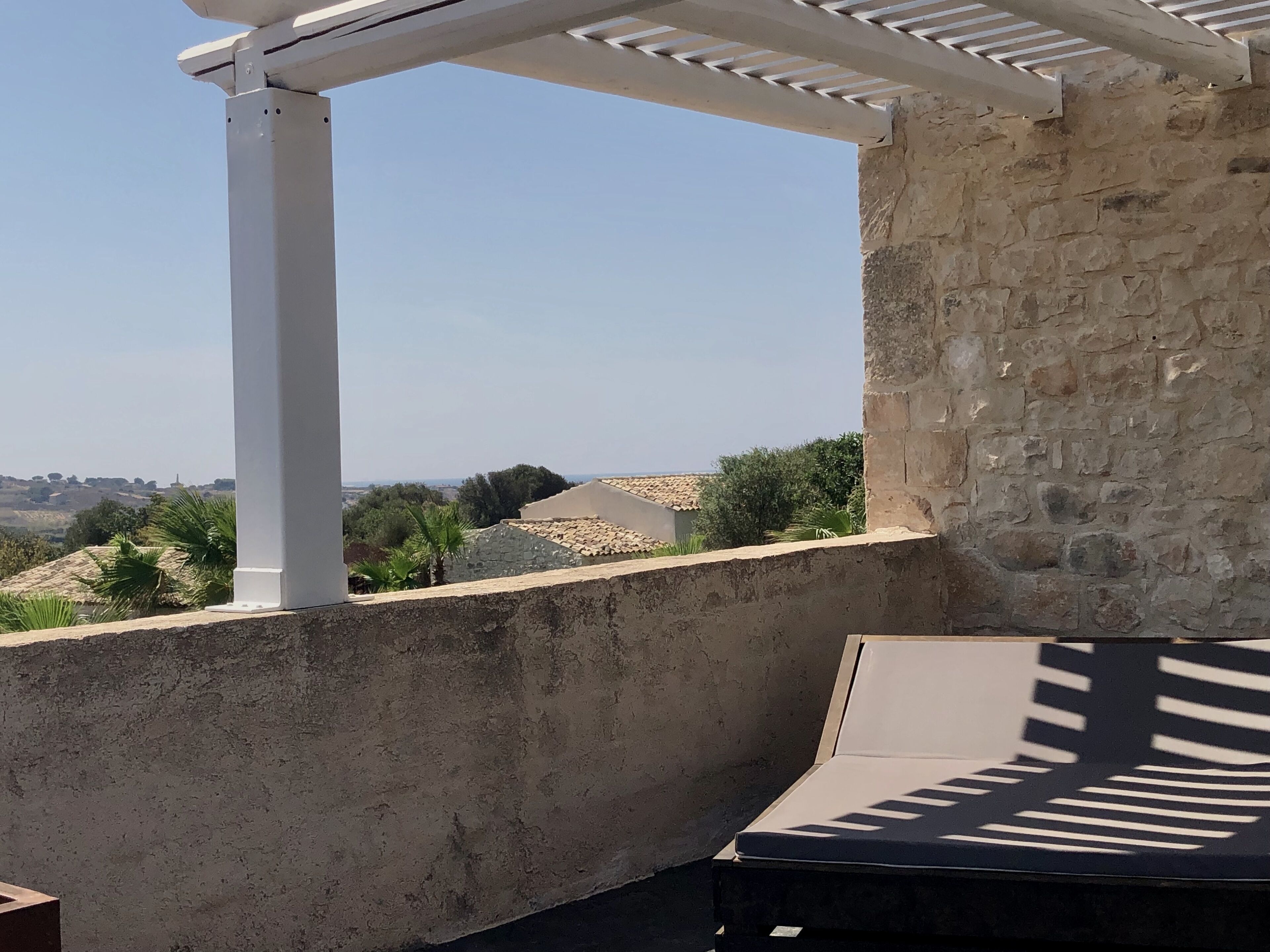 Un mur de pierre surmonté d’une structure de pergola blanche.