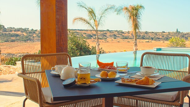 Une table à manger avec des aliments pour le petit-déjeuner, une vue sur une piscine et des palmiers en arrière-plan.