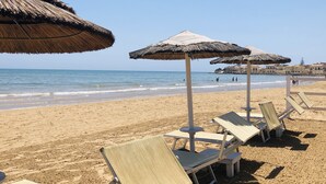 Une plage avec des parasols en chaume et des chaises longues.