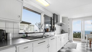 Een moderne keuken met witte kasten, een roestvrijstalen spoelbak en uitzicht op de oceaan door grote ramen.