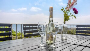 Een tafel met twee wijnglazen, een wijnfles en een bloevas op een balkon met uitzicht op een prachtig landschap.