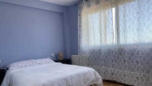 Une chambre à coucher avec un lit, une table de chevet, une lampe et une fenêtre ornée de rideaux à motifs floraux.