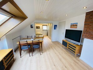 Un espacio habitable compacto con comedor, sofá, televisor y una pared de ladrillo decorativa.