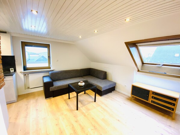 Une pièce de style loft avec un canapé d’angle gris, une petite table noire et un meuble en bois.