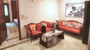 A living room with two red sofas, a coffee table, and a wall clock. - 2 Bed Apartment Sleeps 4 With Parking New Delhi (New Delhi)