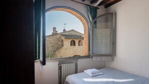 Un dormitorio con cama, ventana con vista a un edificio de piedra y radiador.