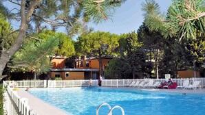 Una piscina con recinzione bianca, circondata da alberi e un edificio con un muretto bianco.