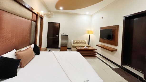 Una camera d'albergo con un letto grande, un divano, una TV fissata al muro e una porta.