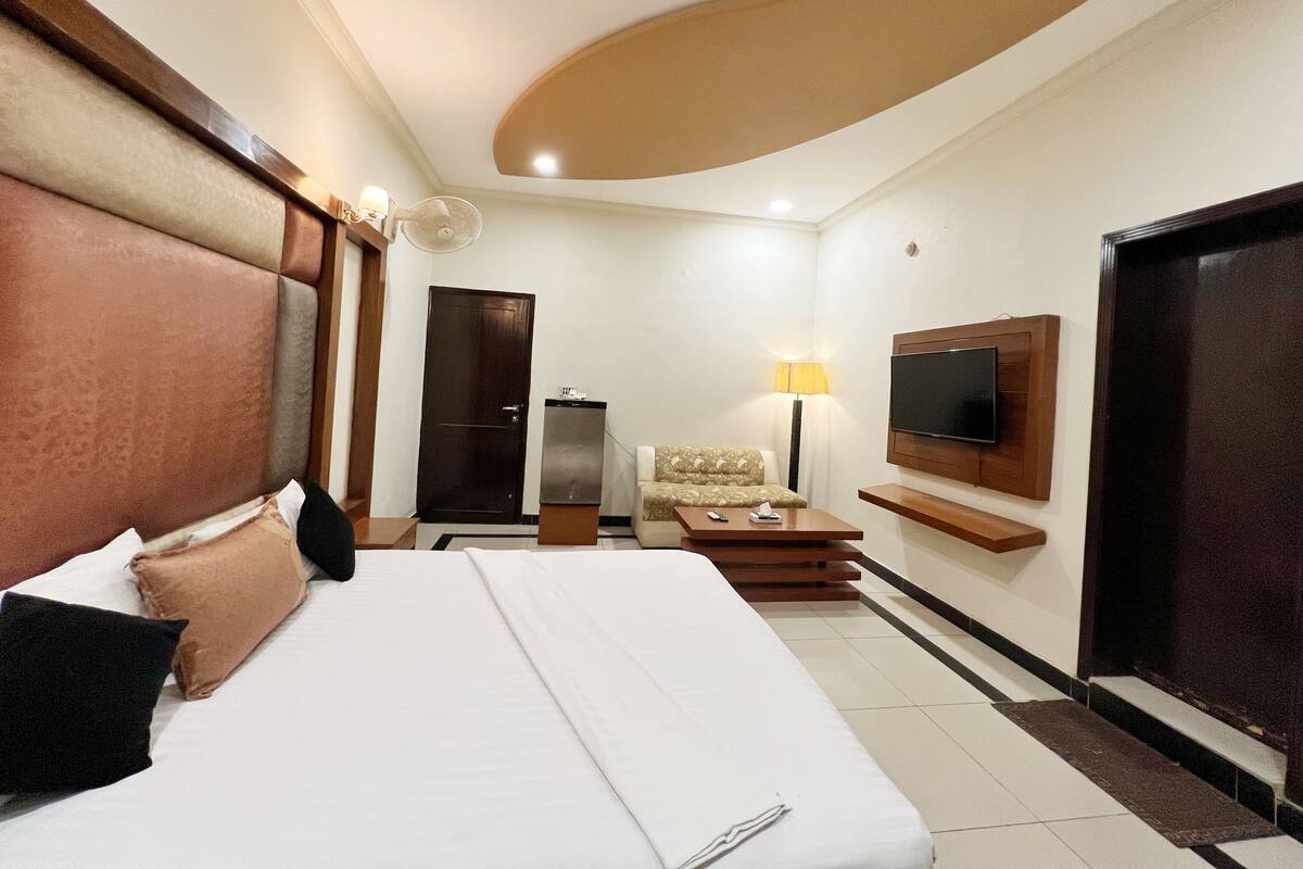 Habitación de hotel con una cama grande, un sofá, un televisor montado en la pared y una puerta.